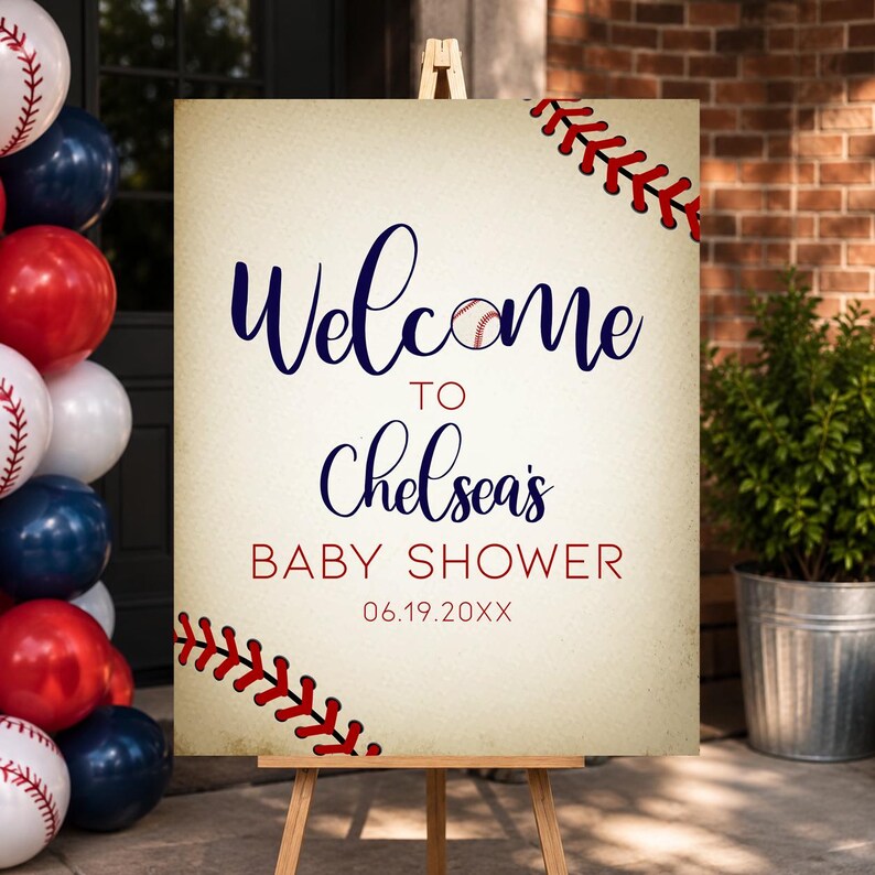 May include: A baseball-themed welcome sign on a wooden easel. The sign reads "Welcome to Chelsea's Baby Shower" in navy blue script, with a baseball graphic. Red baseball stitching accents the corners. Balloons in red, white, and blue are visible.