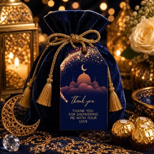 Peut inclure: Une pochette &agrave; cordon en velours bleu profond avec des pompons en cordon dor&eacute; et une &eacute;tiquette cadeau rectangulaire. L'&eacute;tiquette pr&eacute;sente un croissant de lune, une silhouette de mosqu&eacute;e et le texte : thank you, THANK YOU FOR SHOWERING ME WITH YOUR LOVE.