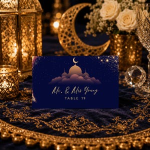 May include: A rectangular navy blue table card featuring a gold crescent moon and mosque silhouette graphic with starry accents. The text reads Mr. & Mrs. Young and TABLE 19 in gold lettering, centered against a dark blue background with a starry sky.