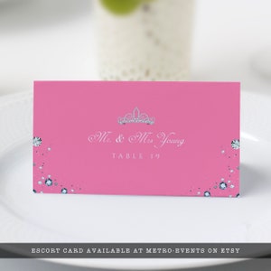 May include: Pink escort card with a silver tiara and the text "Mr. & Mrs. Young" and "Table 19" printed in white.