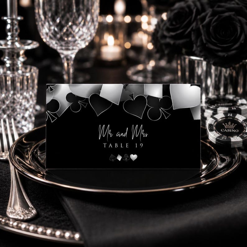 Op de afbeelding: Een rechthoekige zwart-witte tafelkaart met een casinothema en speelkaartsymbolen zoals schoppen, klaveren, ruiten en harten. De tekst luidt Mr and Mrs TABLE 19 in een wit script en schreeflettertype tegen een donkere achtergrond.