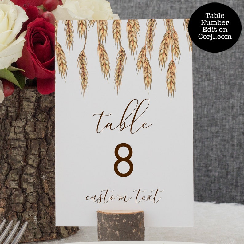May include: White table number card with a brown wheat design at the top. The card says "table 8" in brown text and "custom text" in brown cursive text.