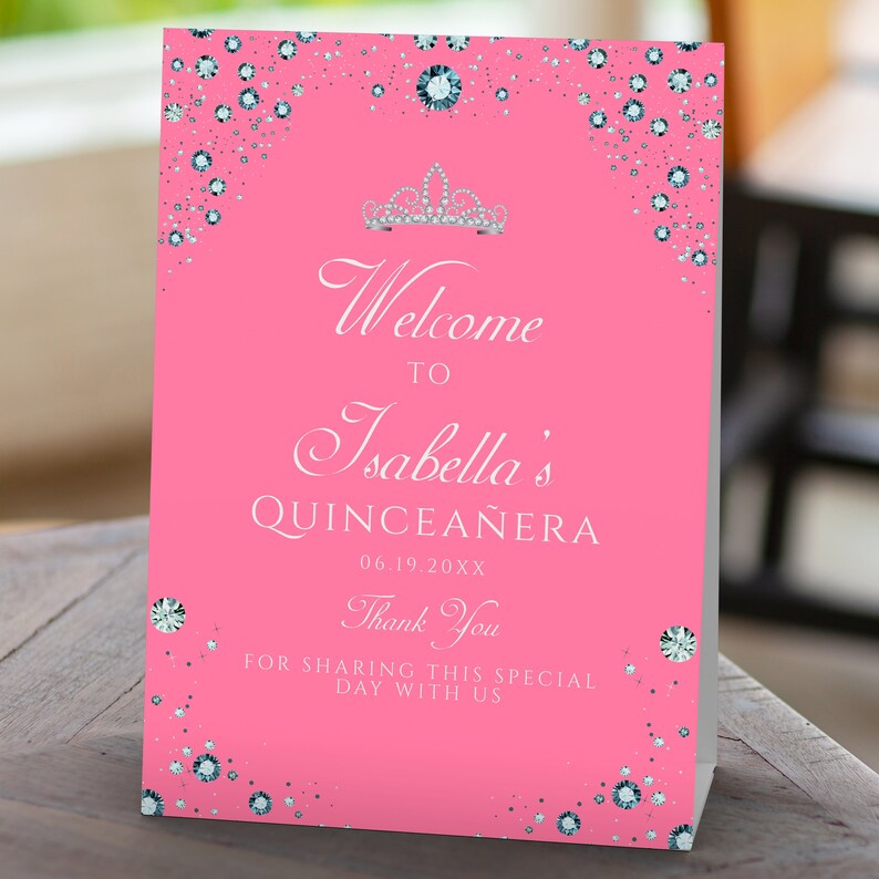 May include: Pink welcome sign with silver glitter and a silver crown. The sign says "Welcome to Isabella's Quincea&ntilde;era 06.19.20XX Thank You for sharing this special day with us".