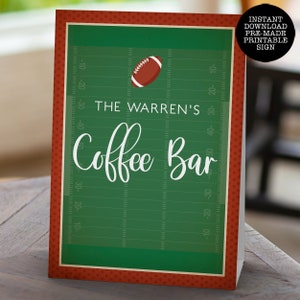 May include: A rectangular sign featuring a green football field background with yard line markings, a brown football graphic, and white text that reads THE WARREN'S Coffee Bar. The sign has a dark red border with a small polka dot pattern.