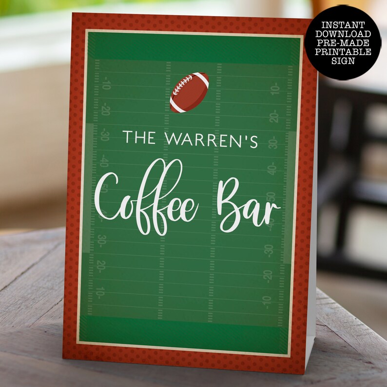 May include: A rectangular sign featuring a green football field background with yard line markings, a brown football graphic, and white text that reads THE WARREN'S Coffee Bar. The sign has a dark red border with a small polka dot pattern.
