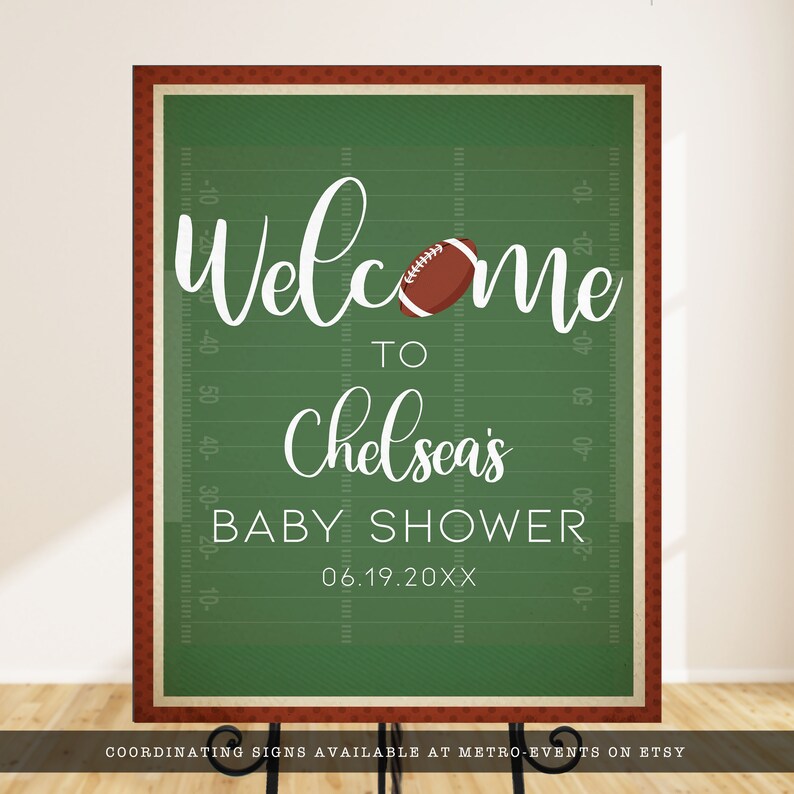 May include: A rectangular sign with a green football field background, white yard line markings, and a brown football graphic. The text reads: Welcome to Chelsea's BABY SHOWER 06.19.20XX. The sign has a dark red border with a small white dot pattern.