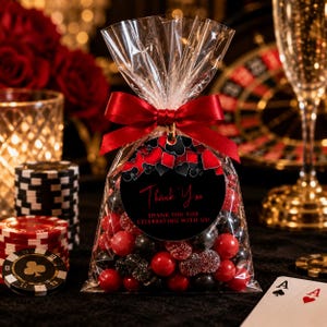 May include: A clear plastic favor bag filled with red and black candies, tied with a red satin ribbon. A round black tag features red and black card suit icons and the text Thank You, THANK YOU FOR CELEBRATING WITH US! in red and white lettering.