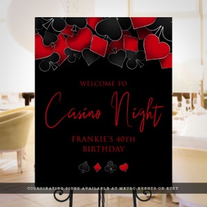 May include: A rectangular black sign featuring a top border of red and black playing card suits including hearts, diamonds, clubs, and spades. The text reads WELCOME TO Casino Night FRANKIE'S 40TH BIRTHDAY with four small card suit icons below.