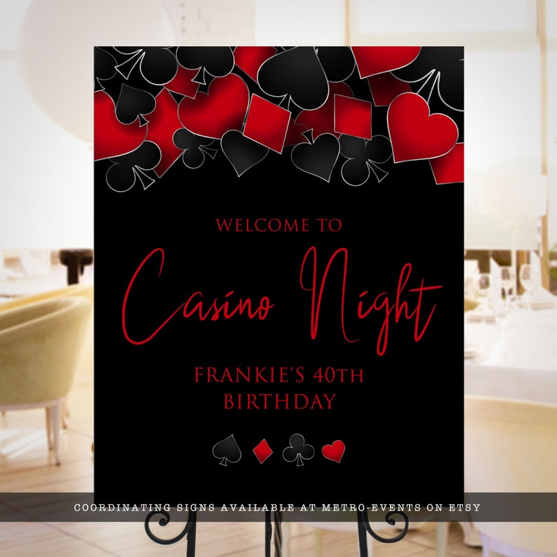 May include: A rectangular black sign featuring a top border of red and black playing card suits including hearts, diamonds, clubs, and spades. The text reads WELCOME TO Casino Night FRANKIE'S 40TH BIRTHDAY with four small card suit icons below.