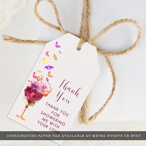 Może przedstawiać: Biała etykieta prezentowa z akwarelowym wzorem kieliszka do wina i kolorowych motyli. Etykieta głosi "Thank You" i "Thank you for showering me with your love" w bordowym skrypcie. Etykieta jest przymocowana sznurkową kokardą.