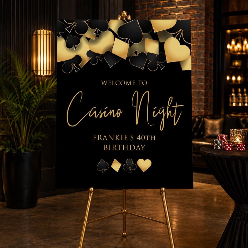 May include: A rectangular black sign on a gold easel featuring gold and black playing card suit symbols at the top and bottom. The text reads: WELCOME TO Casino Night FRANKIE'S 40TH BIRTHDAY. The design includes gold script lettering for the event title.