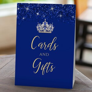 May include: Blue and gold card and gift sign with a glitter background and a crown with blue jewels. The sign says "Cards and Gifts".