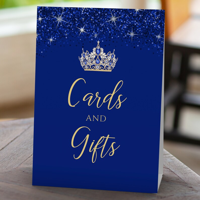 May include: Blue and gold card and gift sign with a glitter background and a crown with blue jewels. The sign says "Cards and Gifts".