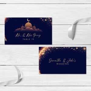 May include: Two rectangular navy blue cards with gold text and accents. One card features a gold mosque silhouette under a crescent moon with the text Mr. & Mrs. Young TABLE 19. The other card displays gold glittery star patterns and the text Samantha & Jake's WEDDING.