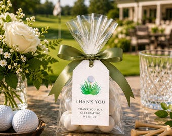 Peut inclure: Un sachet cadeau en cellophane transparent rempli de bonbons ronds blancs, noué avec un ruban de satin vert olive. Une étiquette rectangulaire blanche présente une balle de golf sur un tee dans l'herbe et le texte : THANK YOU THANK YOU FOR CELEBRATING WITH US!
