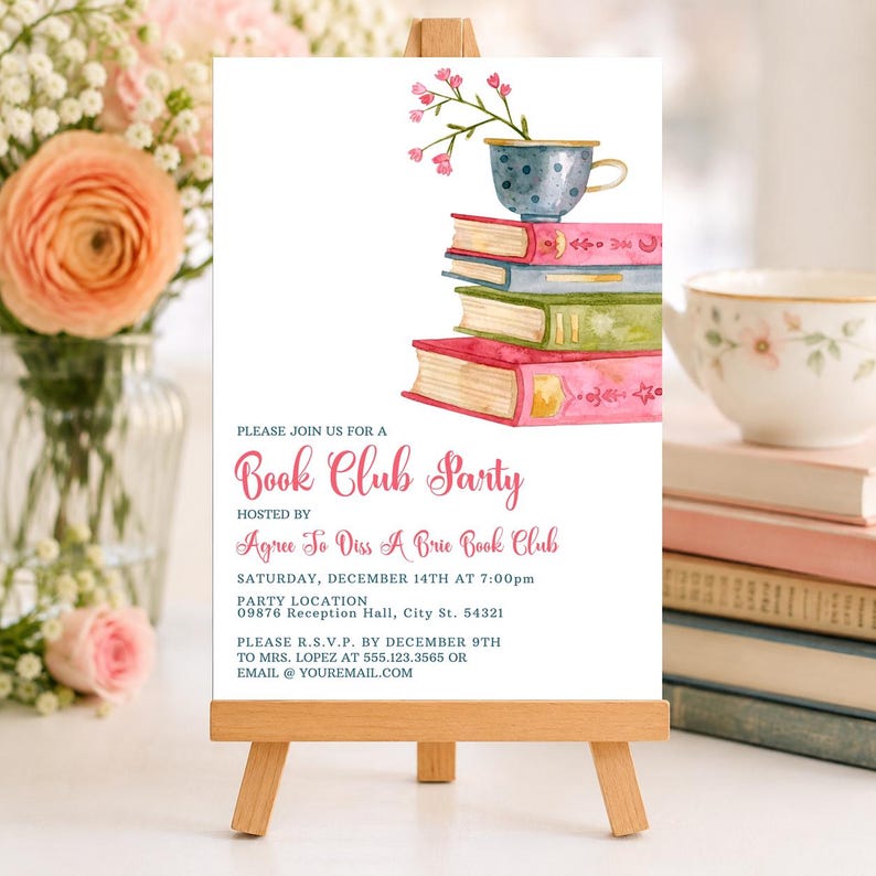 May include: A white invitation card on a wooden easel featuring a watercolor illustration of a blue teacup with pink flowers resting on a stack of four colorful books. The text reads: Please join us for a Book Club Party hosted by Agree To Diss A Brie Book Club, Saturday, December 14th at 7:00pm, party location 09876 Reception Hall, City St. 54321, please R.S.V.P. by December 9th to Mrs. Lopez at 555.123.3565 or email @ youremail.com.