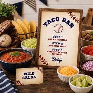 Puede incluir: Un letrero enmarcado con el texto TACO BAR, STEP 1 GRAB A TORTILLA, STEP 2 ADD SOME MEAT, STEP 3 DRESS IT UP WITH TOPPINGS y Enjoy, decorado con gr&aacute;ficos de b&eacute;isbol. Una peque&ntilde;a tarjeta a juego dice MILD SALSA, colocada cerca de cuencos de comida.