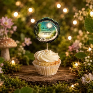 Op de afbeelding: Een cupcake met witte glazuur in een wit papieren vormpje, bekroond met een ronde decoratie op een houten prikker. De decoratie toont een donker boslandschap met een maansikkel, fonkelende lichtjes en de tekst Thank You THANK YOU FOR CELEBRATING WITH US!