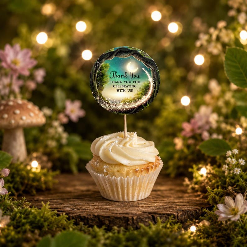 Op de afbeelding: Een cupcake met witte glazuur in een wit papieren vormpje, bekroond met een ronde decoratie op een houten prikker. De decoratie toont een donker boslandschap met een maansikkel, fonkelende lichtjes en de tekst Thank You THANK YOU FOR CELEBRATING WITH US!