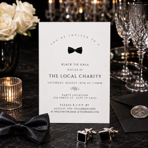May include: A white rectangular invitation card with black text and a small black bow tie graphic. The text reads: You're invited to a Black Tie Gala hosted by The Local Charity on Saturday, August 14th at 7:00pm, with RSVP details included.