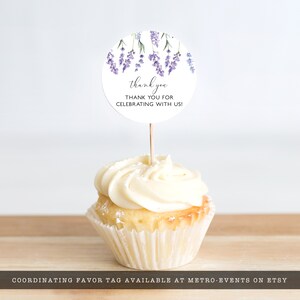 May include: A white cupcake with vanilla frosting topped with a round lavender-themed thank you tag. The tag says "thank you" and "THANK YOU FOR CELEBRATING WITH US!"