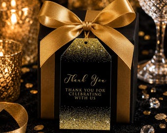 Peut inclure: Une boîte cadeau noire entourée d'un large ruban de satin doré noué en boucle. Une étiquette cadeau rectangulaire noire est suspendue au ruban, avec des paillettes dorées en haut et en bas et le texte Thank You THANK YOU FOR CELEBRATING WITH US.