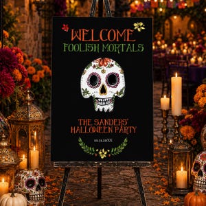 May include: A black rectangular sign on an easel featuring the text WELCOME FOOLISH MORTALS in orange and green, a central white sugar skull illustration, the text THE SANDERS' HALLOWEEN PARTY, and the date 10.31.20XX above a green leaf garland.