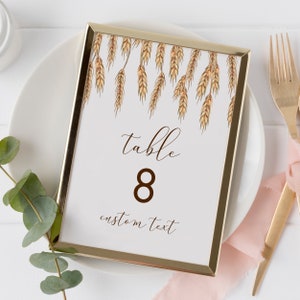 May include: A gold-framed table number card with a watercolor illustration of wheat stalks. The card reads "table 8 custom text".