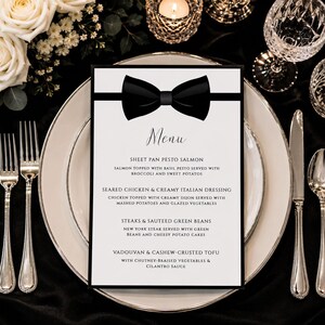 May include: A rectangular white menu card featuring a black bow tie graphic at the top. The text lists food items including sheet pan pesto salmon, seared chicken with creamy Italian dressing, steaks with sauteed green beans, and vadouvan cashew-crusted tofu.