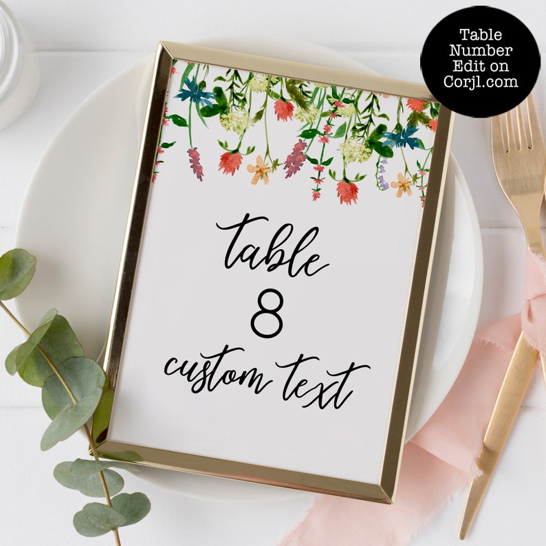 Pode incluir: Um cart&atilde;o de n&uacute;mero de mesa com moldura dourada com detalhes florais em aquarela. O cart&atilde;o exibe "Table 8" e "custom text" em uma escrita elegante. A parte superior do cart&atilde;o apresenta um design floral colorido com flores vermelhas, laranja e azul.