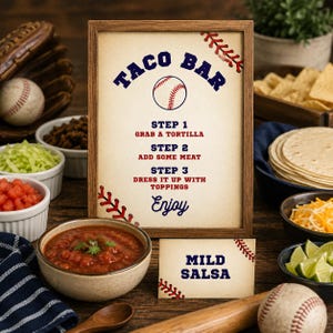 Puede incluir: Un letrero enmarcado con temática de béisbol titulado Taco Bar, con las instrucciones: Step 1 Grab a tortilla, Step 2 Add some meat, Step 3 Dress it up with toppings, Enjoy. Una tarjeta pequeña a juego dice Mild Salsa, ambos con costuras rojas.