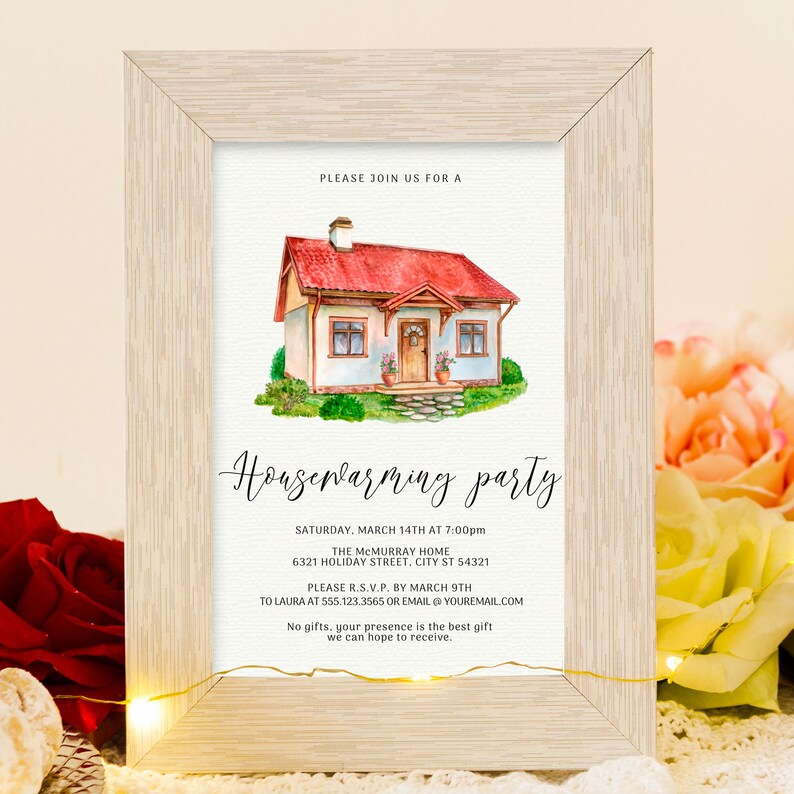 May include: A framed housewarming party invitation. The watercolor illustration depicts a charming house with a red roof and green lawn. The invitation text includes the date, time, location, and RSVP information. The frame is light-colored wood.