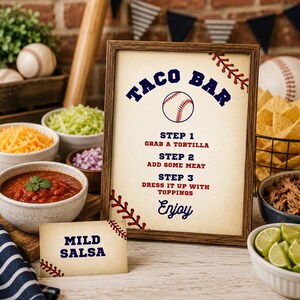 Puede incluir: Un letrero enmarcado con tem&aacute;tica de b&eacute;isbol que dice TACO BAR, STEP 1 GRAB A TORTILLA, STEP 2 ADD SOME MEAT, STEP 3 DRESS IT UP WITH TOPPINGS y Enjoy. Una peque&ntilde;a tarjeta a juego dice MILD SALSA. El dise&ntilde;o presenta costuras de b&eacute;isbol rojas.