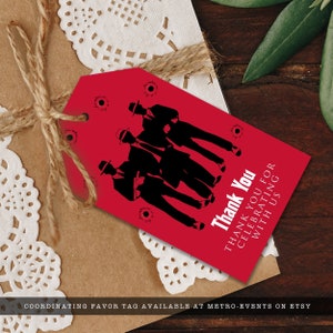 K&ouml;nnte beinhalten: Roter Geschenkanh&auml;nger mit einer Silhouette von vier M&auml;nnern in Anz&uuml;gen und H&uuml;ten. Der Anh&auml;nger hat Einschussl&ouml;cher und den Text "Thank You THANK YOU FOR CELEBRATING WITH US".