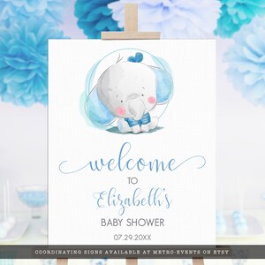 May include: A baby shower welcome sign featuring a watercolor illustration of a cute baby elephant in blue. The sign says "welcome to Elizabeth's BABY SHOWER 07.29.20XX". The sign is displayed on a wooden easel.
