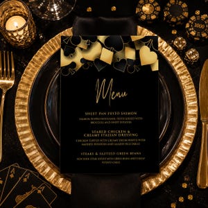May include: A black menu card with gold text and a top border featuring gold and black playing card suit symbols. The text reads Menu, Sheet Pan Pesto Salmon, Seared Chicken & Creamy Italian Dressing, and Steaks & Sauteed Green Beans.