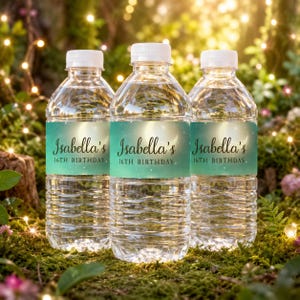 Op de afbeelding: Drie doorzichtige plastic waterflessen met witte doppen, elk voorzien van een blauwgroen label met een halve maan en de tekst Isabella's 16TH BIRTHDAY. De labels hebben een verloopontwerp met kleine witte sterren op een donkerblauwe achtergrond.