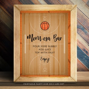 May include: A framed rectangular sign featuring a basketball court graphic with an orange basketball icon. The text reads: Mom-osa Bar, POUR SOME BUBBLY, ADD JUICE, TOP WITH FRUIT, Enjoy! The sign is displayed in a light wood frame on a surface.