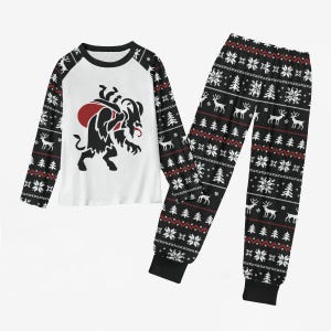 May include: A two-piece pyjama set consisting of a long-sleeved top and matching trousers. The top features a white central panel with a black and red Krampus graphic, while the sleeves and trousers display a black, white and red Nordic-style pattern.