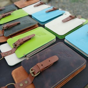May include: A collection of rectangular leather pouches in various colors including lime green, sky blue, white, and dark brown. Each pouch features a brown leather strap with a metal buckle closure and a debossed logo reading MIRAKU.