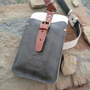 May include: A dark olive green leather pouch with a white interior lining, featuring a tan leather strap with a brass buckle closure. The front is embossed with a griffin logo and the text MIRAKI. A matching adjustable leather shoulder strap is attached.