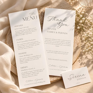 Könnte beinhalten: Eine weiße Hochzeitsmenükarte mit der Überschrift The Menu, eine Dankeskarte mit der Aufschrift Thank You to our family and friends und ein kleines Namensschild für Serena Johnson. Der Text enthält ein Drei-Gänge-Menü, Dankesworte und das Datum 12.12.2027.