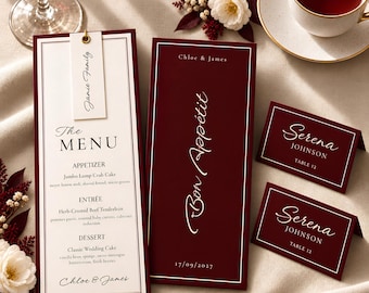May include: A wedding stationery set featuring a tall menu card with a white centre and burgundy border, a matching burgundy menu cover with the text Bon Appétit and Chloe & James, and two burgundy place cards with the name Serena Johnson and Table 12.