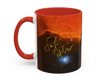 Könnte beinhalten: Ein Keramikbecher mit rotem Henkel und rotem Innenraum, der außen mit einem Weltraum-Nebel-Motiv bedruckt ist. Die Oberfläche zeigt eine leuchtend orange und dunkelbraune kosmische Wolke mit Sternen und dem gelben kursiven Text Set Astro.