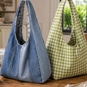 May include: Two hobo bags standing side by side. The left bag is constructed from blue denim panels with a blue and white floral interior lining. The right bag features a green and white gingham check pattern throughout the exterior and interior.