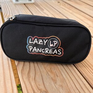 May include: A black rectangular zippered pouch featuring a colorful graphic print on the front. The text reads LAZY PANCREAS with the letters LP inside a circle. The design has a gradient outline transitioning from blue to orange and red.