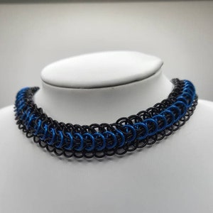 May include: A black and blue chainmail choker necklace. The necklace is made of small metal rings that are interlocked to create a chainmail pattern. The necklace is approximately 16 inches long and has a lobster clasp closure.
