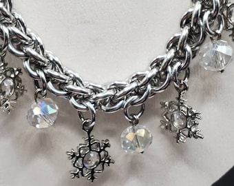 May include: A silver chain necklace with snowflake charms and crystal beads. The necklace is a winter-themed design.