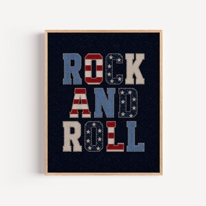 May include: A framed wall art print featuring the text ROCK AND ROLL in a block font. The letters are filled with patterns of red and white stripes and white stars on a blue background, set against a dark navy blue textured background.