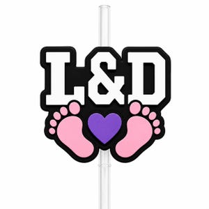 May include: A silicone straw topper featuring the white text L&D on a black background, positioned above two light pink baby footprints and a central purple heart. The topper is attached to a clear, transparent plastic drinking straw.